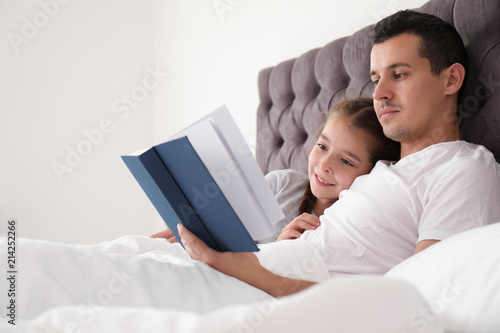 Father reading book with child in bedroom. Happy family