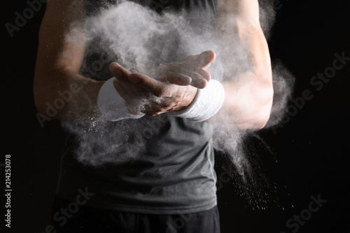 Young man applying chalk powder on hands against dark background