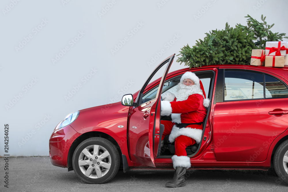 Fototapeta premium Authentic Santa Claus in car with gift boxes and Christmas tree, view from outside