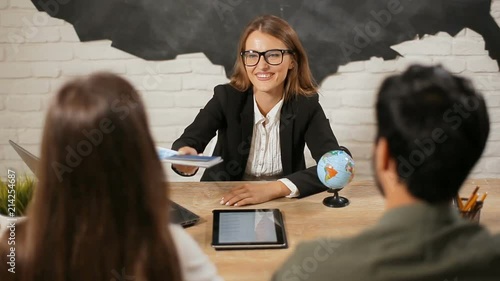 Smiling travel agent giving passports with tickets to happy couple, elegant woman congratulates family couple with upcoming summer vacation by shaking hands