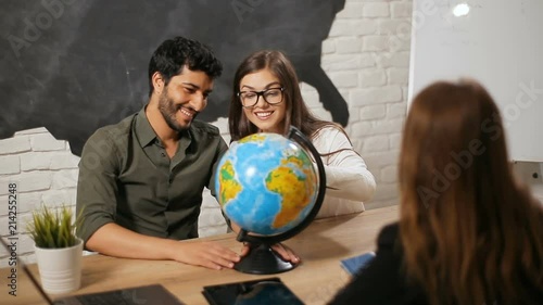 Cheerful young couple choosing country to visit, happy husband turning huge globe when dreaming wife with closed eyes points at the location where they are going to fly