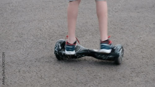 The teenager rides on a self-balancing two-wheeled hoverboard in a circle. Movement on the asphalt. Life style. The legs are close-up. photo