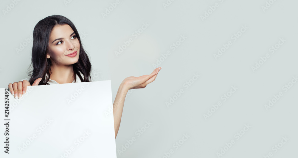 Smiling business woman showing empty open hand and holding white blank paper banner background. Young woman portrait, business and education concept Smiling business woman showing empty open hand and holding white blank paper banner background. Young woman portrait, business and education concept