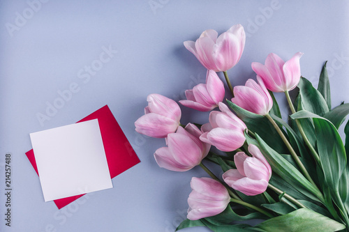 Fototapeta Naklejka Na Ścianę i Meble -  Pink tulips flowers and sheet of paper over light blue background. Greeting card or wedding invitation. Flat lay, top view
