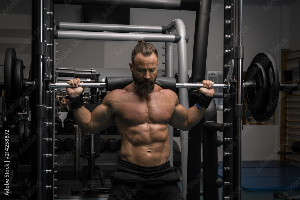 Hombre fuerte con grandes músculos haciendo sentadillas mientras entrena en el gimnasio. Ponerse en forma. Hombre fuerte con grandes músculos haciendo sentadillas mientras entrena en el gimnasio. Ponerse en forma.