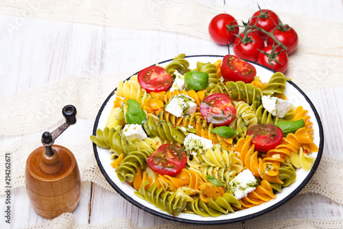 Italian food - Salad with colorful pasta, cherry tomatoes, feta cheese and fresh basil on white wooden background photo