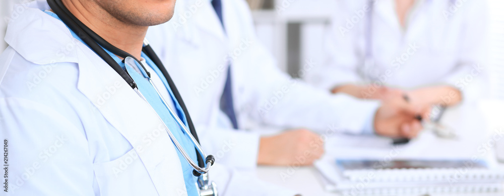 Unknown male doctor is sitting at the table and working in the hospital office. Closeup of stethoscope Unknown male doctor is sitting at the table and working in the hospital office. Closeup of stethoscope