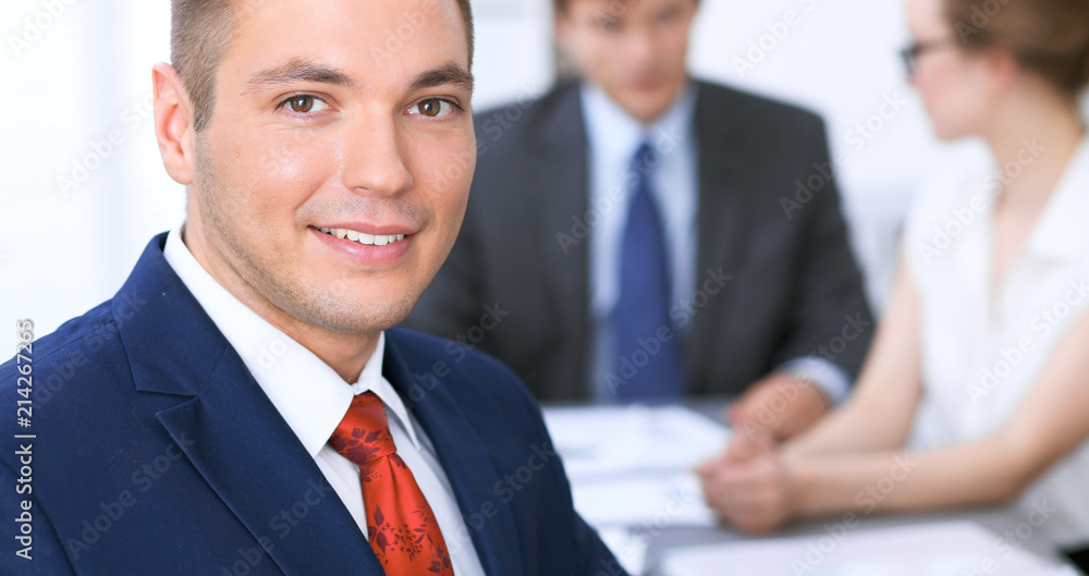 Portrait of cheerful smiling business man against a group of business people at a meeting. Portrait of cheerful smiling business man against a group of business people at a meeting.