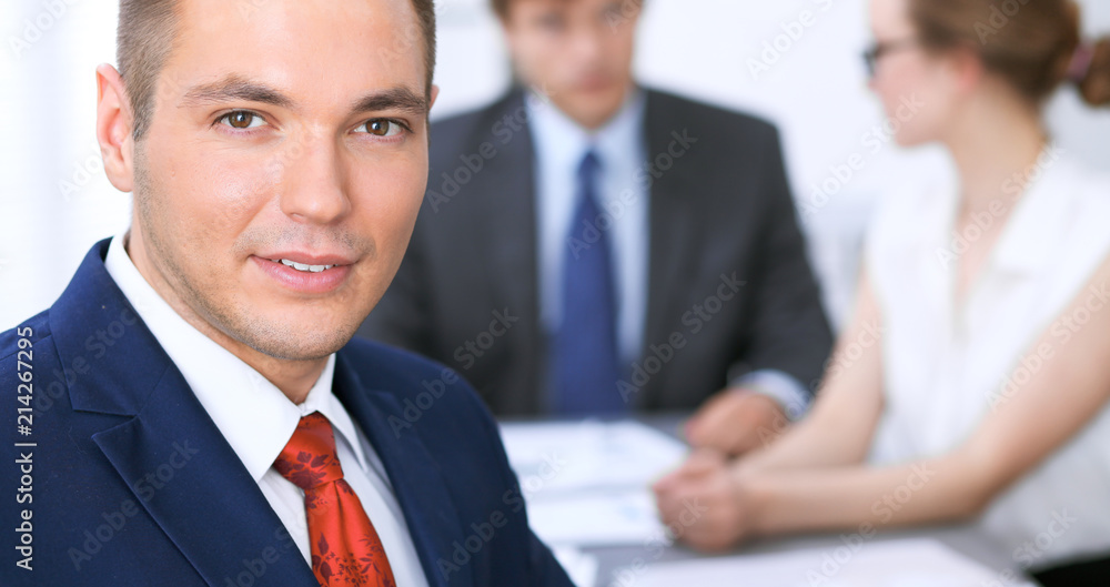 Portrait of cheerful smiling business man against a group of business people at a meeting. Portrait of cheerful smiling business man against a group of business people at a meeting.
