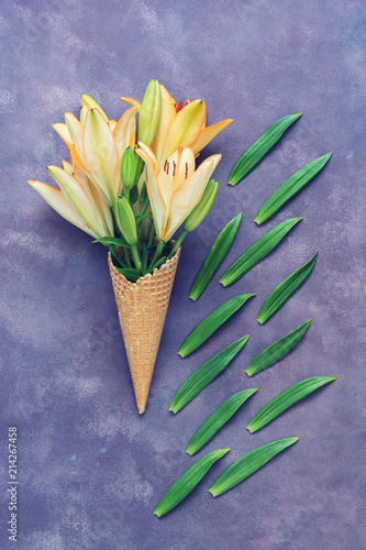 Beautiful composition of flowers on a blue background. Lilies in a waffle cone. Flat lay.
