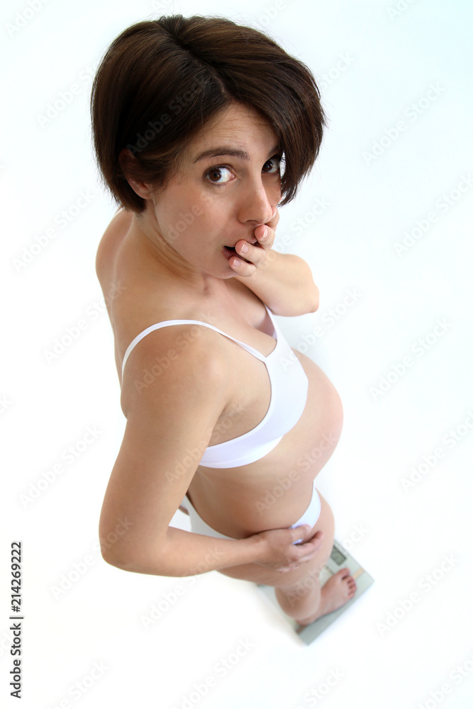 Schwanger Frau steht auf einer Waage und schaut erstaunt Schwanger Frau steht auf einer Waage und schaut erstaunt