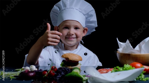 Little master chef at the kitchen table, surrounded with cooking products, showing thumb photo