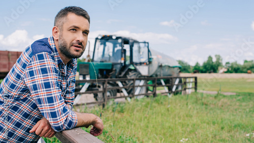 Tela handsome middle aged farmer leaning at fence and looking away at farm