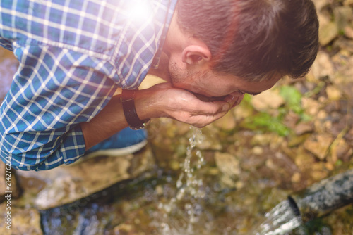 a young man in a blue shirt drinking clean water from an underground source
