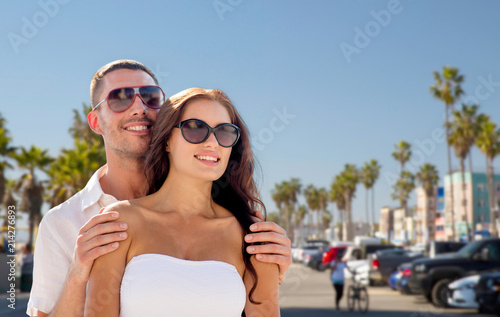 travel, tourism and relationships concept - happy smiling couple in sunglasses over venice beach background in california