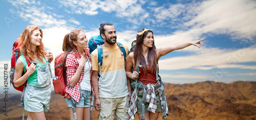 travel, tourism, hike and adventure concept - group of smiling friends with backpacks pointing finger to something over grand canyon national park hills background