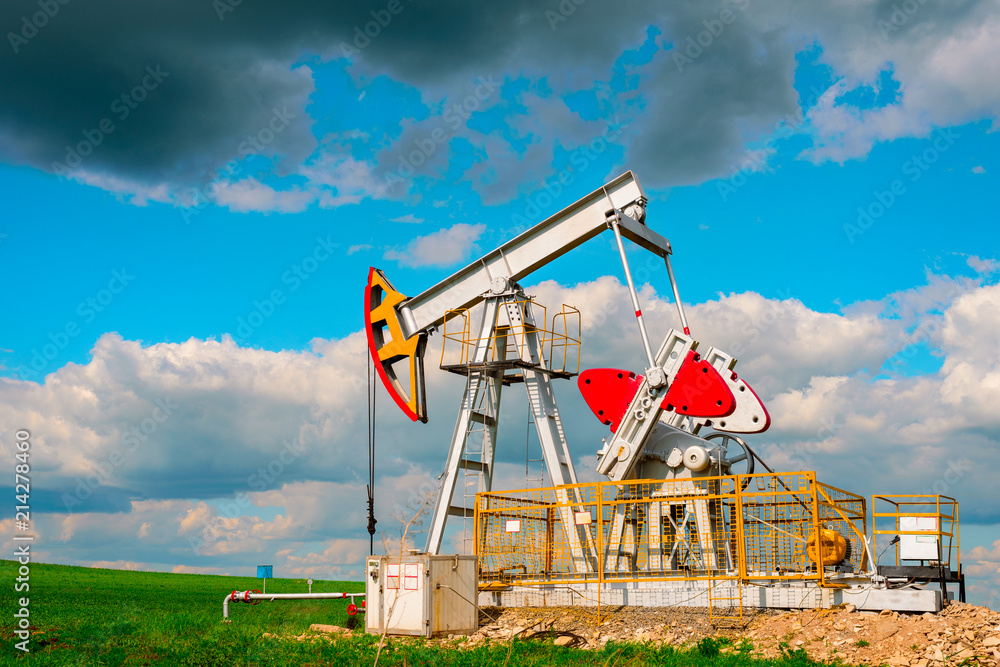 Oil pump tower in the field with green grass with blue cloudy sky Oil pump tower in the field with green grass with blue cloudy sky