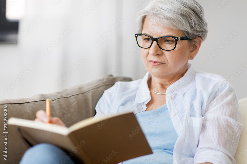 age, leisure and people concept - close up of senior woman in glasses writing to notebook or diary at home - obrazy, fototapety, plakaty 