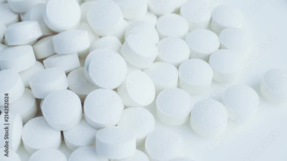 White tablets, pills dropping on white table. Closeup, white background. Concept of pharmaceuticals; meds, drugs, pharmacology, materia medica. Closeup. Macro shot. White tablets, pills dropping on white table. Closeup, white background. Concept of pharmaceuticals; meds, drugs, pharmacology, materia medica. Closeup. Macro shot.