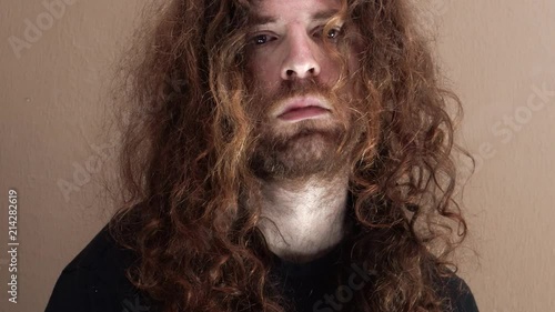 Long Auburn Haired Man with beard stares depressingly into camera isolated alone in room one person close up photo