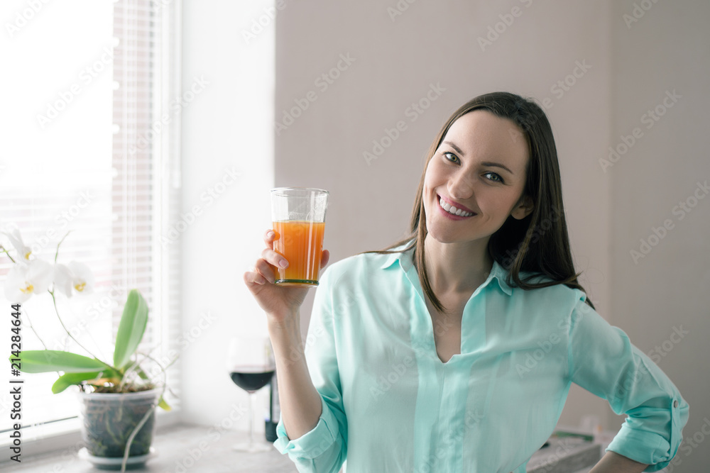 Woman at the window in the kitchen, smiling and holding a glass of juice Woman at the window in the kitchen, smiling and holding a glass of juice