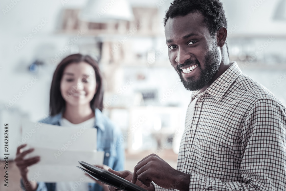 Digital device. Cheerful handsome positive man holding a tablet and looking at you while being in a great mood Digital device. Cheerful handsome positive man holding a tablet and looking at you while being in a great mood