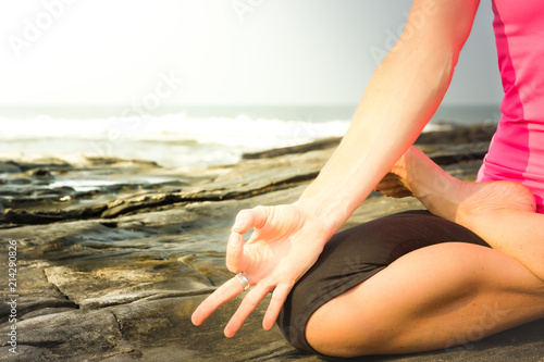 Female yogi hand practicing meditation on the rocks by the sea at sunrise. Yoga teacher in padmasana on the beach. Instructor on lotus pose, chin mudra, peaceful mindfulness concept