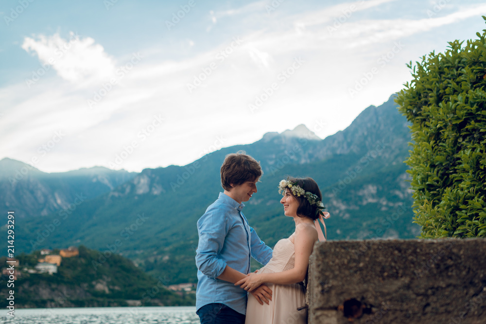 Happy man hugging his pregnant wife outdoors near the lake Como. Pregnant couple. Summer day