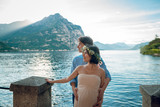 Close up of happy young couple. Pregnant woman with her husband standing near the beautiful lake Como with mountain on background in the evening