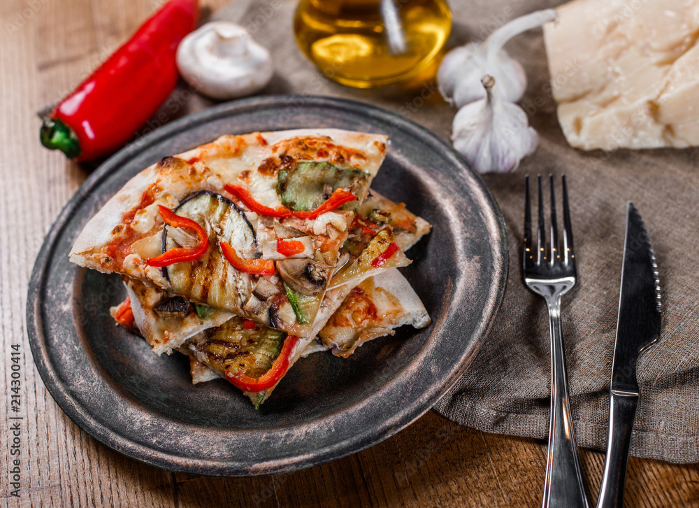 Sliced pizza with chicken, zucchini, eggplant, pepper, cheese and mushrooms on the plate vintage. Top view. Toning. Sliced pizza with chicken, zucchini, eggplant, pepper, cheese and mushrooms on the plate vintage. Top view. Toning.