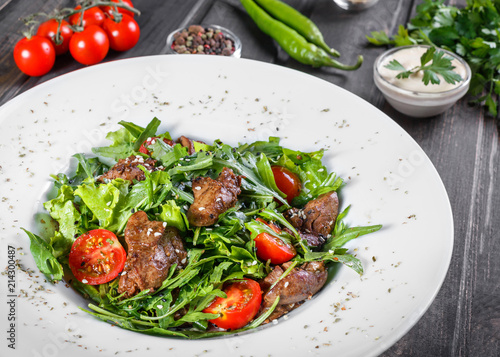 Hot salad with fried liver, cherry tomatoes and mixed greens on dark wooden background. Healthy food. Ingredients on table.