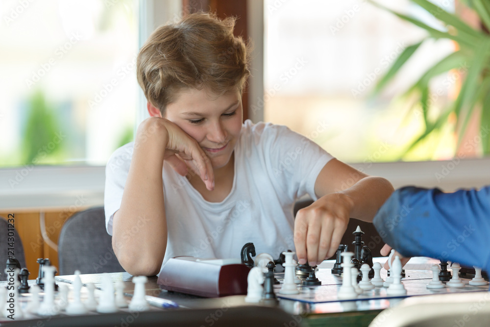 cute handsome boy in white tshirt plays chess with his rival in chess class. Education concept, intellectual game. Chess tournament, lesson, camp, training concept