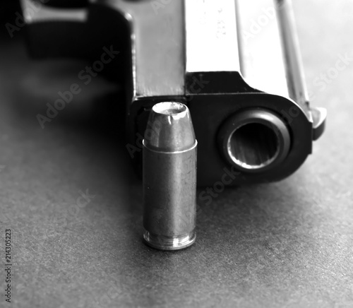 A single 40 caliber hollow point bullet standing next to the muzzle of a black pistol on a black background shown in black and white