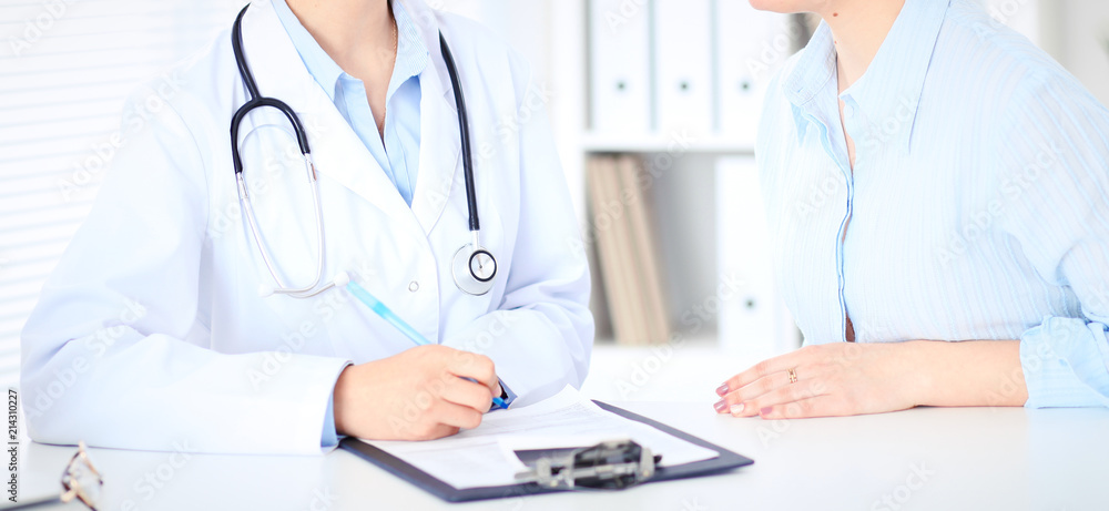Unknown female doctor and patient discussing something while sitting at the table at hospital. Medicine and healthcare concepts Unknown female doctor and patient discussing something while sitting at the table at hospital. Medicine and healthcare concepts