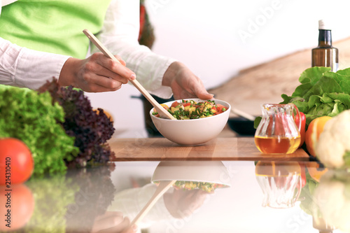 Fototapeta Naklejka Na Ścianę i Meble -  Close Up of human hands cooking vegetable salad in kitchen on the glass table with reflection. Healthy meal, and vegetarian food concept