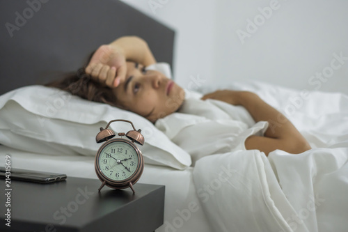 Asian woman lying in bed late at night with retro alarm clock, young female sleep in bedroom at home. insomnia sleeping, worried and stressed concepts photo