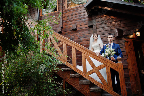 Beautiful wedding couple posing on stairs of wooden chalet outdoor.