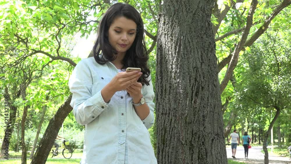 Portrait casual girl using social media on smartphone in the park standing smile Portrait casual girl using social media on smartphone in the park standing smile