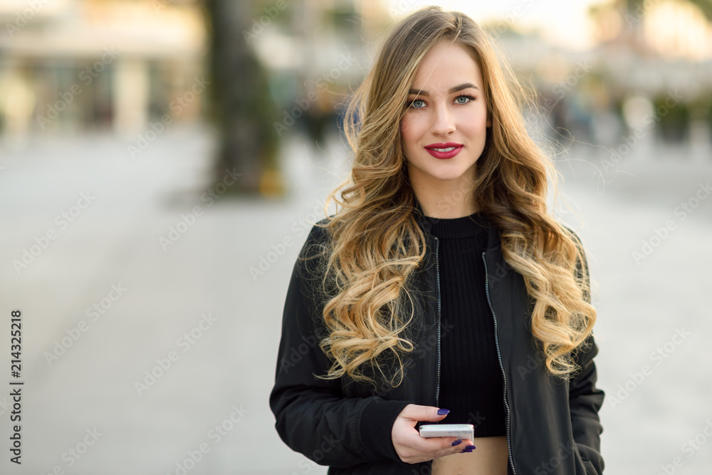 Fototapeta premium Blonde woman texting with her smartphone in urban background
