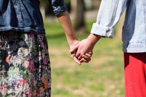 Two young women in walking holding her hands in urban park.
