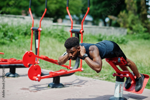 African american male athlete sport man with running sports arm case for mobile phone, doing exercises on the street workout simulators.