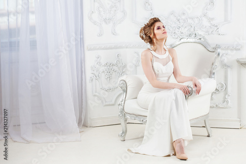 Wedding style. Beautiful young bride sitting in luxury chair in luxurious light interior.