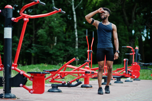 African american male athlete sport man with running sports arm case for mobile phone, posed against street workout simulators.