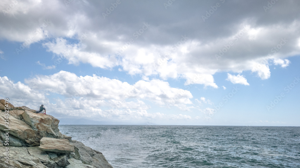 Lonely girl on a rock cliff, observing the ocean