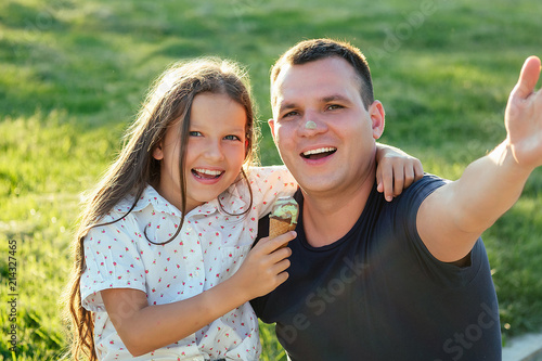 beautiful long-haired little girl toothy smile long hair eating pistachio tasty ice cream and photograph themselves selfie on the phone with father in the park heat summer trip.
