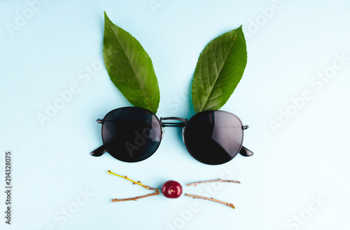 Rabbit of cherry, sunglasses, branches and green leaves on a blue background photo