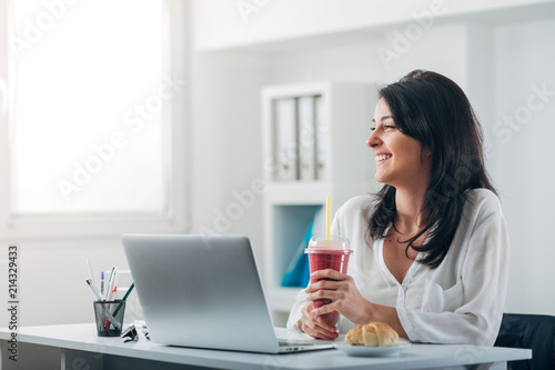 Attractive Woman Drinking Smoothie at the Office and Laughing