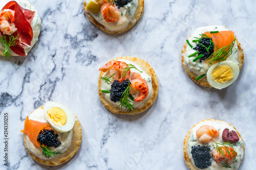 Selection of cocktail blinis with salmon, cured bresaola, crayfish, caviar, quail eggs and sour cream - gourmet party food - top view photo