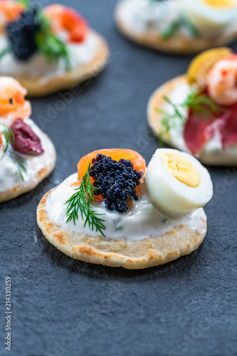 Selection of cocktail blinis with salmon, cured bresaola, crayfish, caviar, quail eggs and sour cream - gourmet party food.