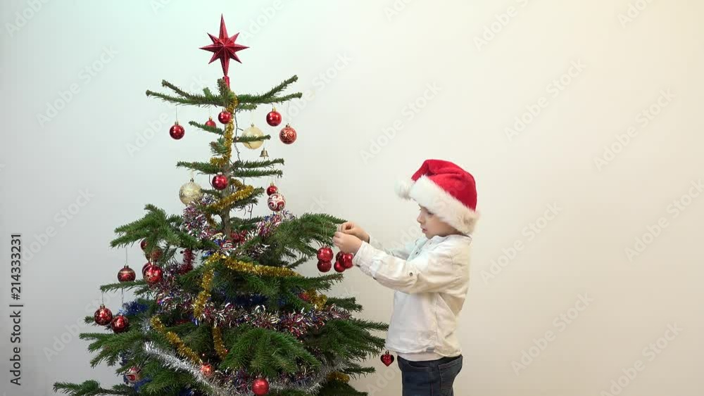 Adorable child with Santa clause cap decorating Christmas tree Adorable child with Santa clause cap decorating Christmas tree
